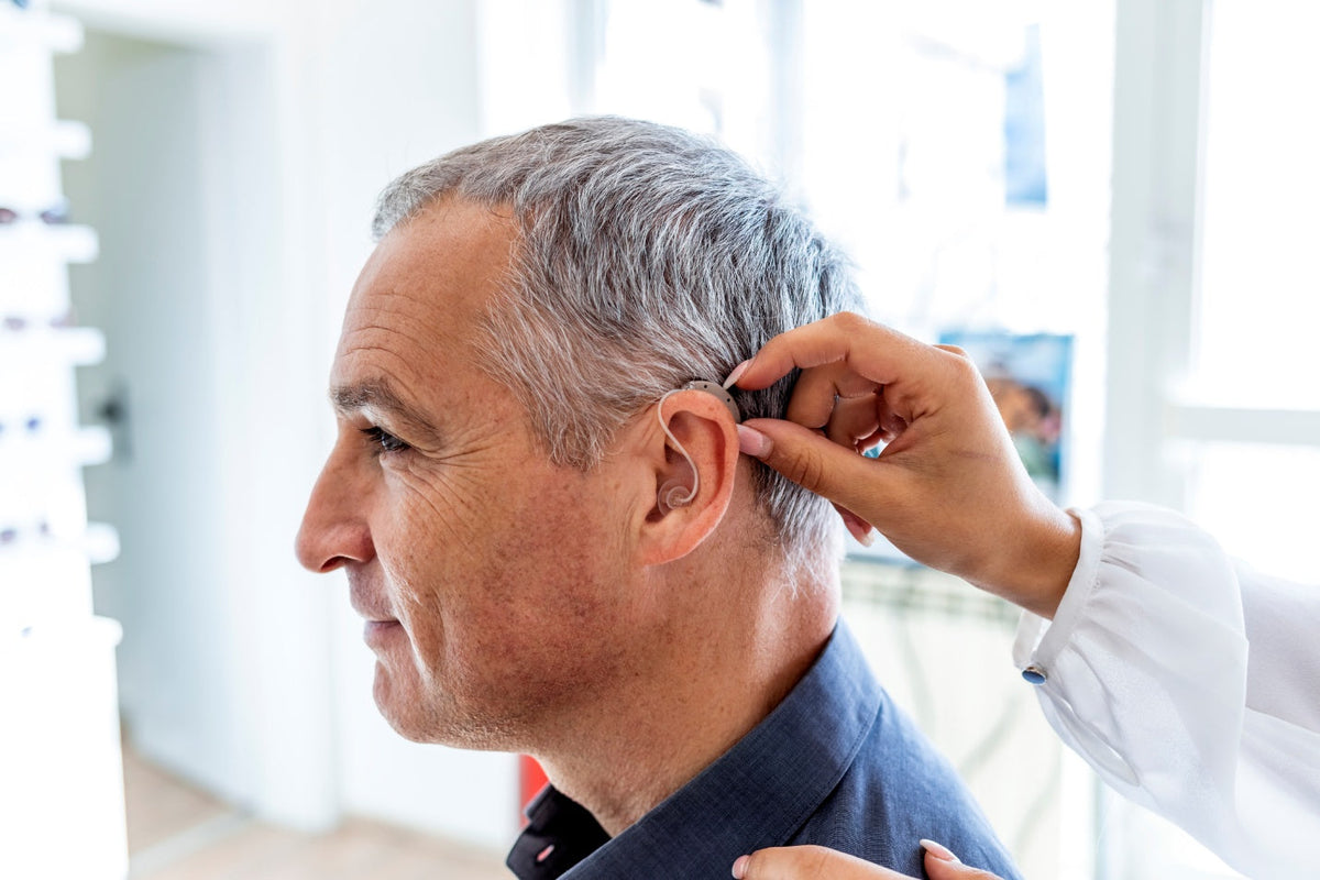 Audiologist fitting a behind-the-ear hearing aid on a senior patient in Canada