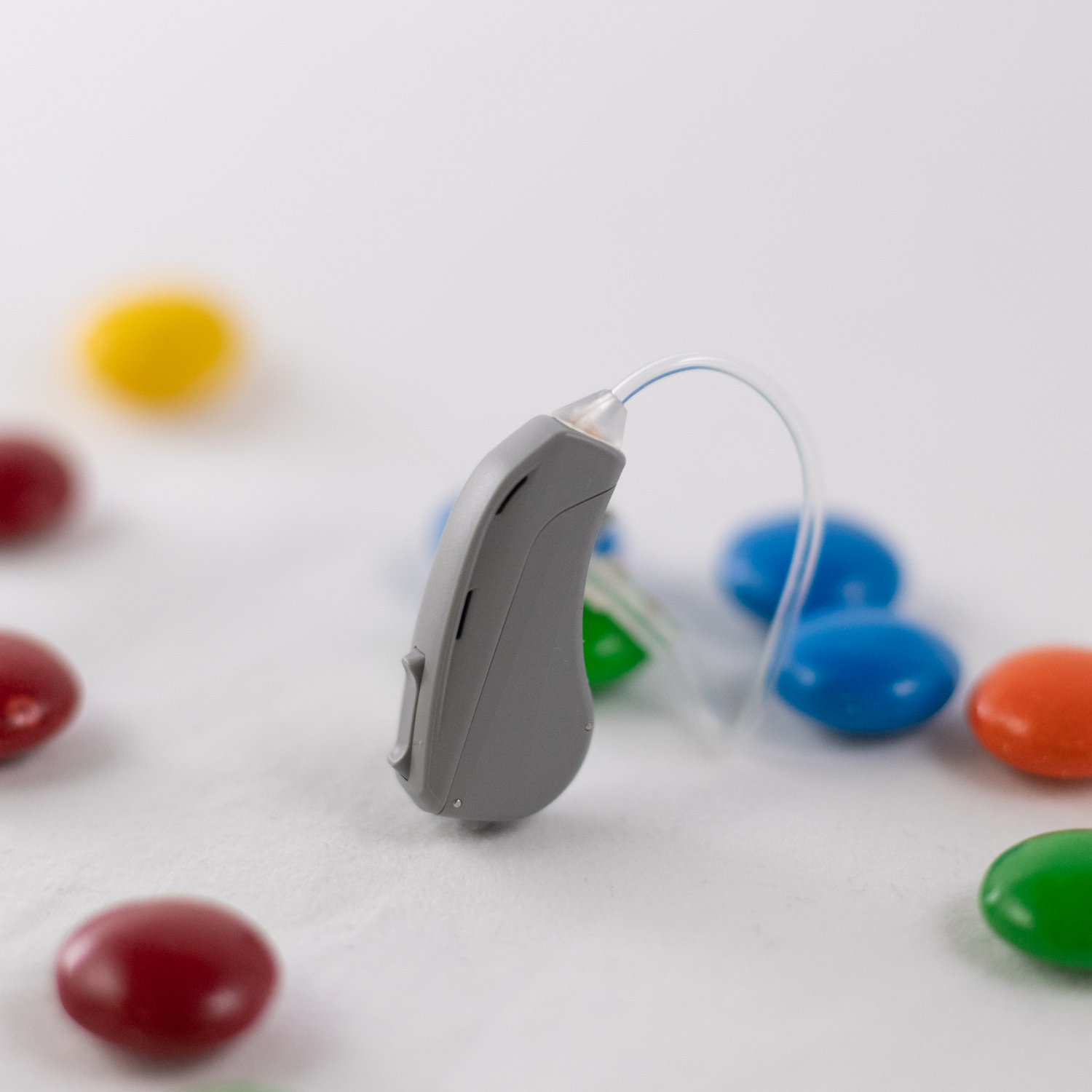 A Warbler Series 3 Hearing Aid on a table, surrounded by small colourful candies to show of how small the hearing aid is